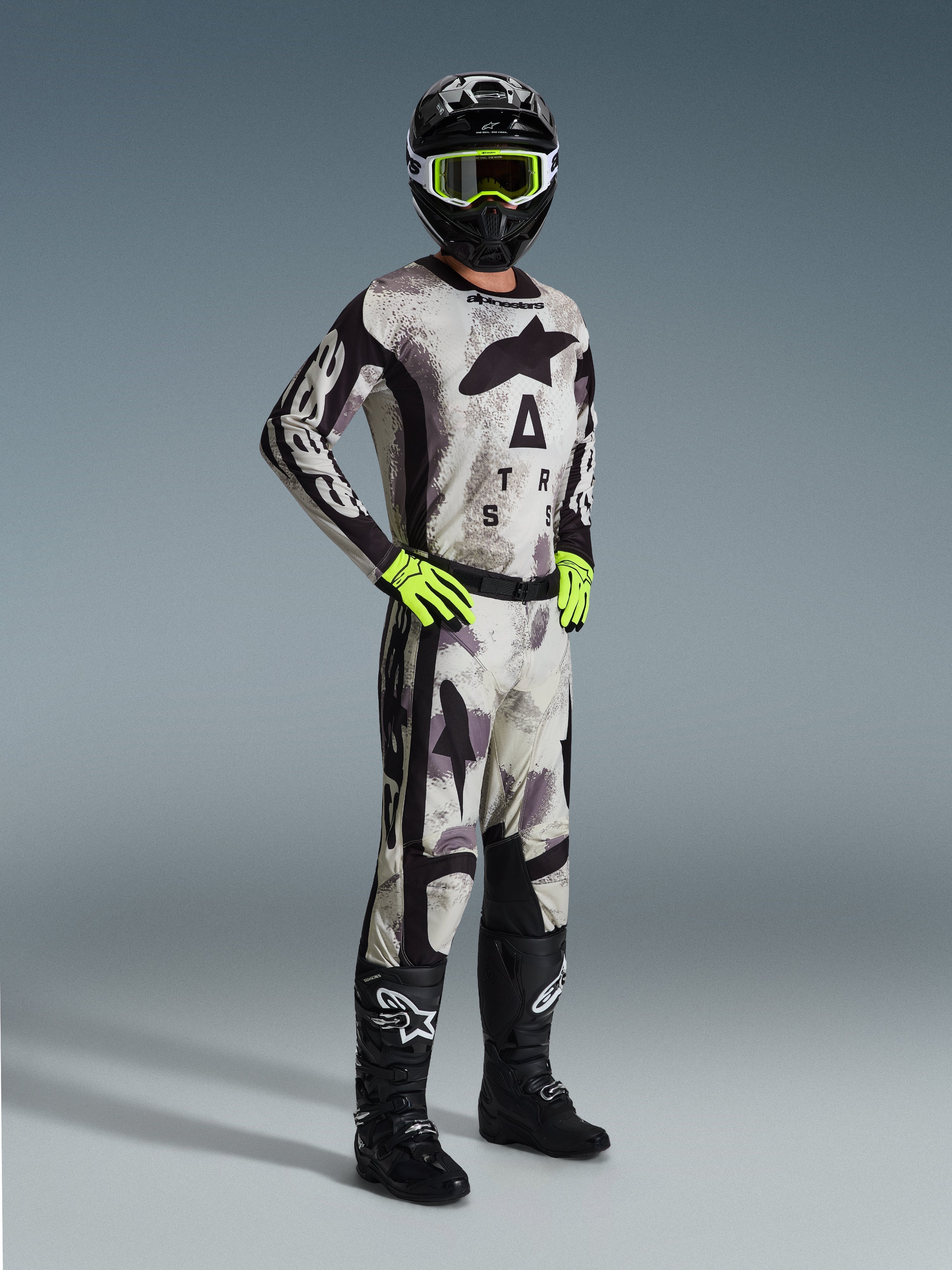 Motocrossförare klädd i 2026 Racer Lahnd Jersey i Sand Camo, grått och svart kamouflagemönster med Alpinestars-branding, matchande motocrossbyxor, neongula handskar, svart hjälm med gula goggles och svarta stövlar, komplett professionell outfit för offroad-racing.