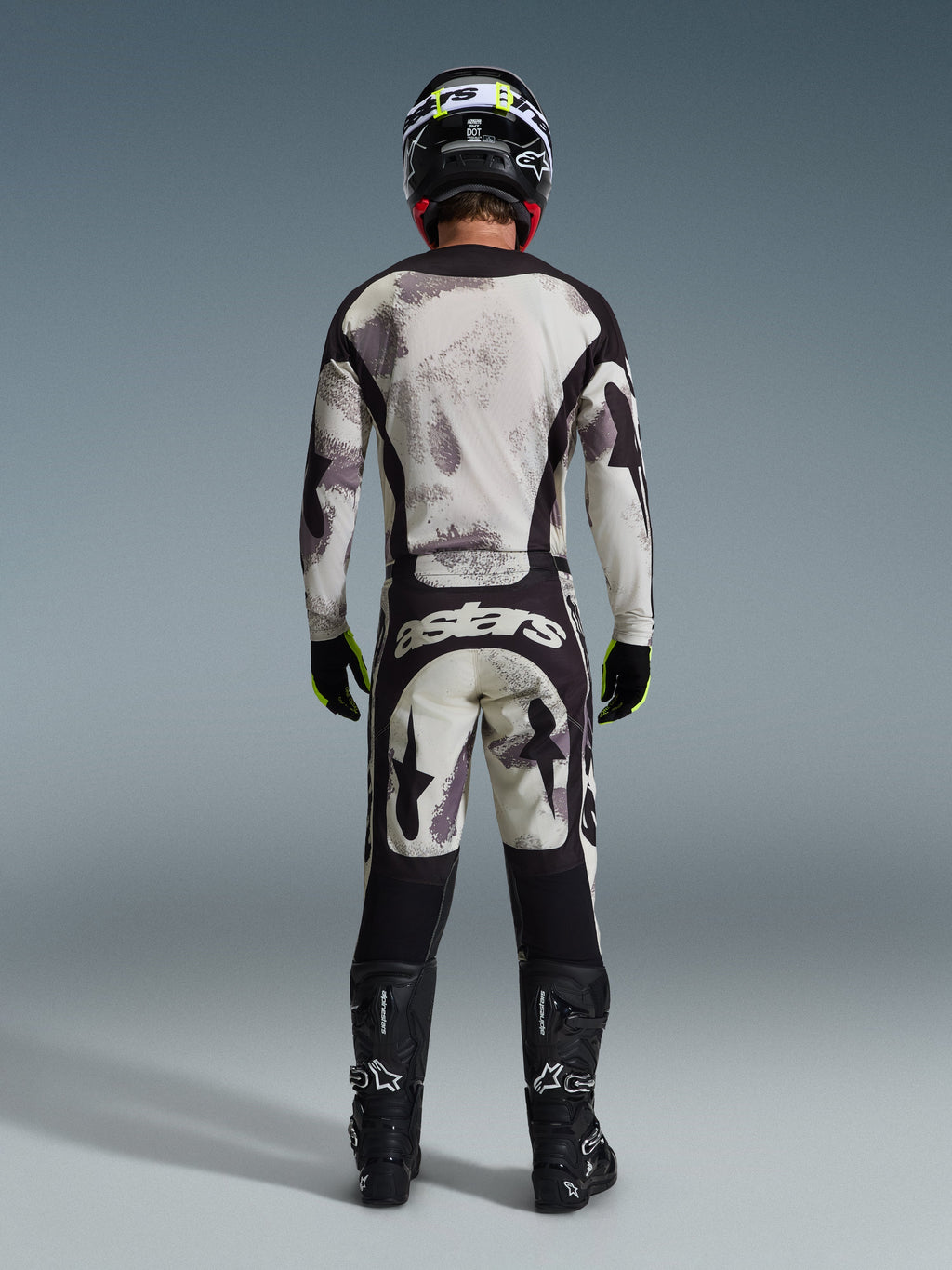Motocrossförare sedd bakifrån bärande 2026 Racer Lahnd Jersey och matchande byxor i Sand Camo, med ett krämvitt och grått abstrakt mönster med svarta paneler, 'astars'-logotyp på byxorna, matchat med svarta Alpinestars-stövlar och en svart hjälm för en komplett offroad-racinglook.