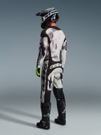 Motocrossförare i komplett racingutrustning, 2026 Racer Lahnd-tröja och matchande byxor i färgen Sand Camo, grått och svart kamouflagemönster med stora Alpinestars-logotyper, svart hjälm, svarta stövlar och neongula handskar, sedd bakifrån.