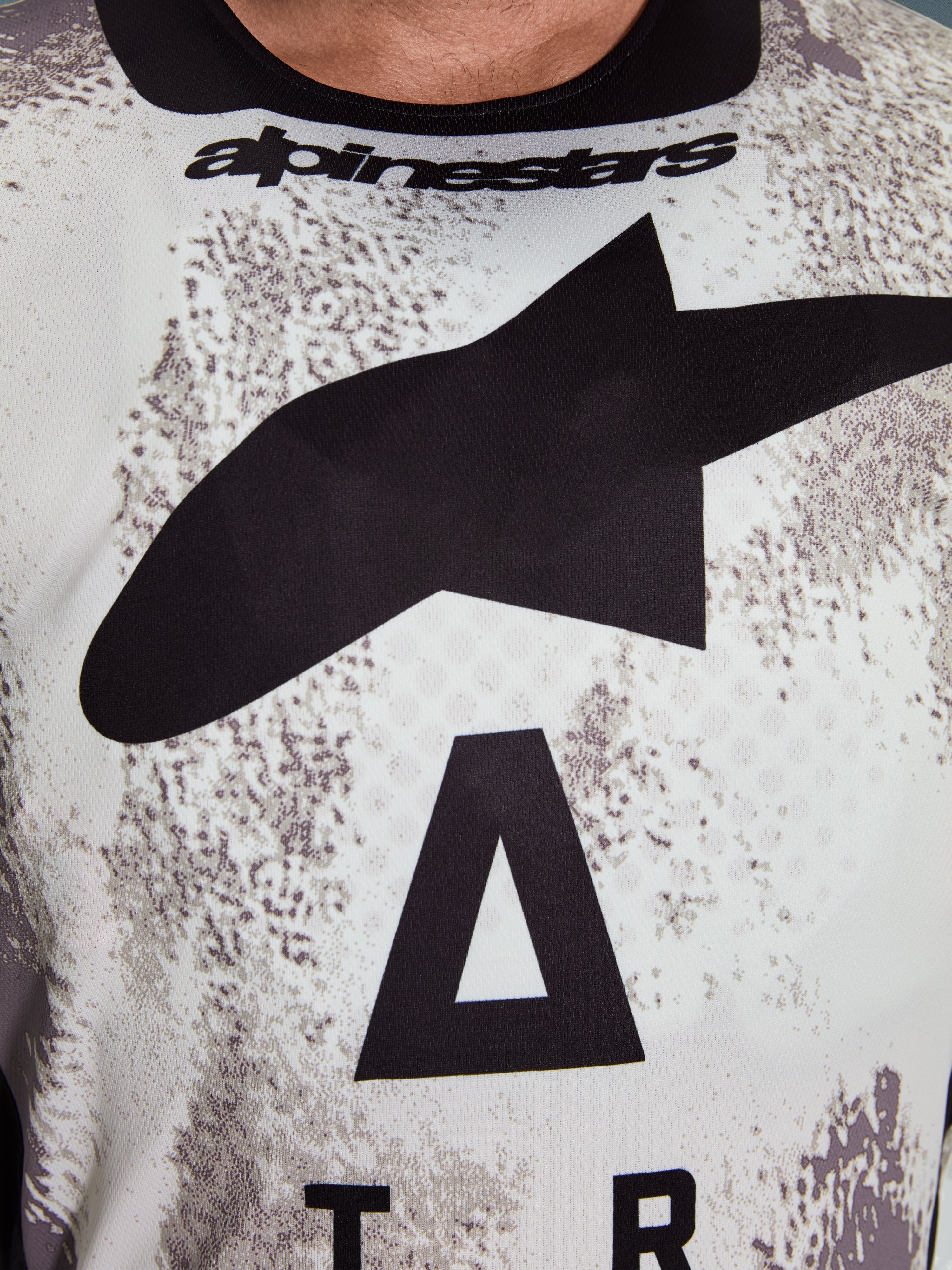 Alpinestars 2026 Racer Lahnd-tröja, närbild på bröstpartiet, Sand Camo-mönster med stor svart stjärnlogotyp och Alpinestars ordmärke, ventilerande tekniskt polyestermaterial för terrängkörning