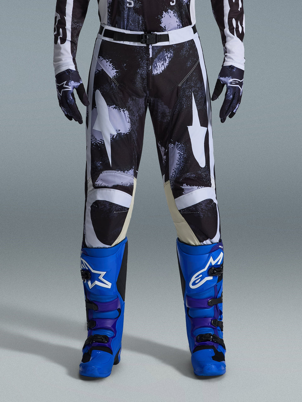 Alpinestars 2026 Racer Lahnd byxor, motocrossbyxor, Iron Camo, bärs med matchande kamouflagehandskar och klarblå och lila stövlar, stiliserad vit stjärngrafik på ett mörkt kamouflagemönster, tekniskt magnetspänne, professionell racingutrustning för terrängkörning