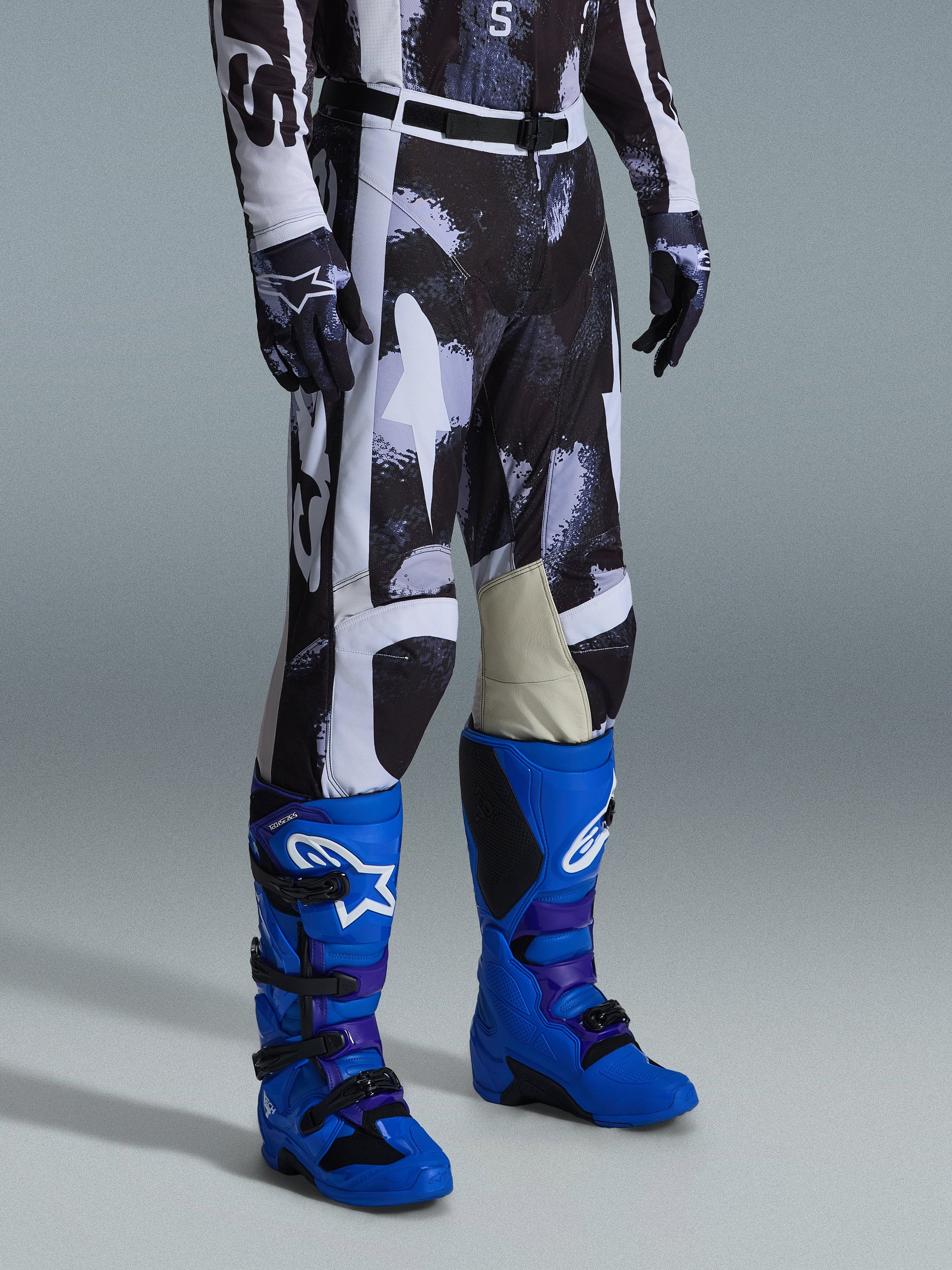 Alpinestars 2026 Racer Lahnd Pants, Motocross Pants, Iron Camo gray and black pattern, worn with bright blue racing boots and matching gloves, featuring white panels and goat leather inner knees, performance-driven off-road gear