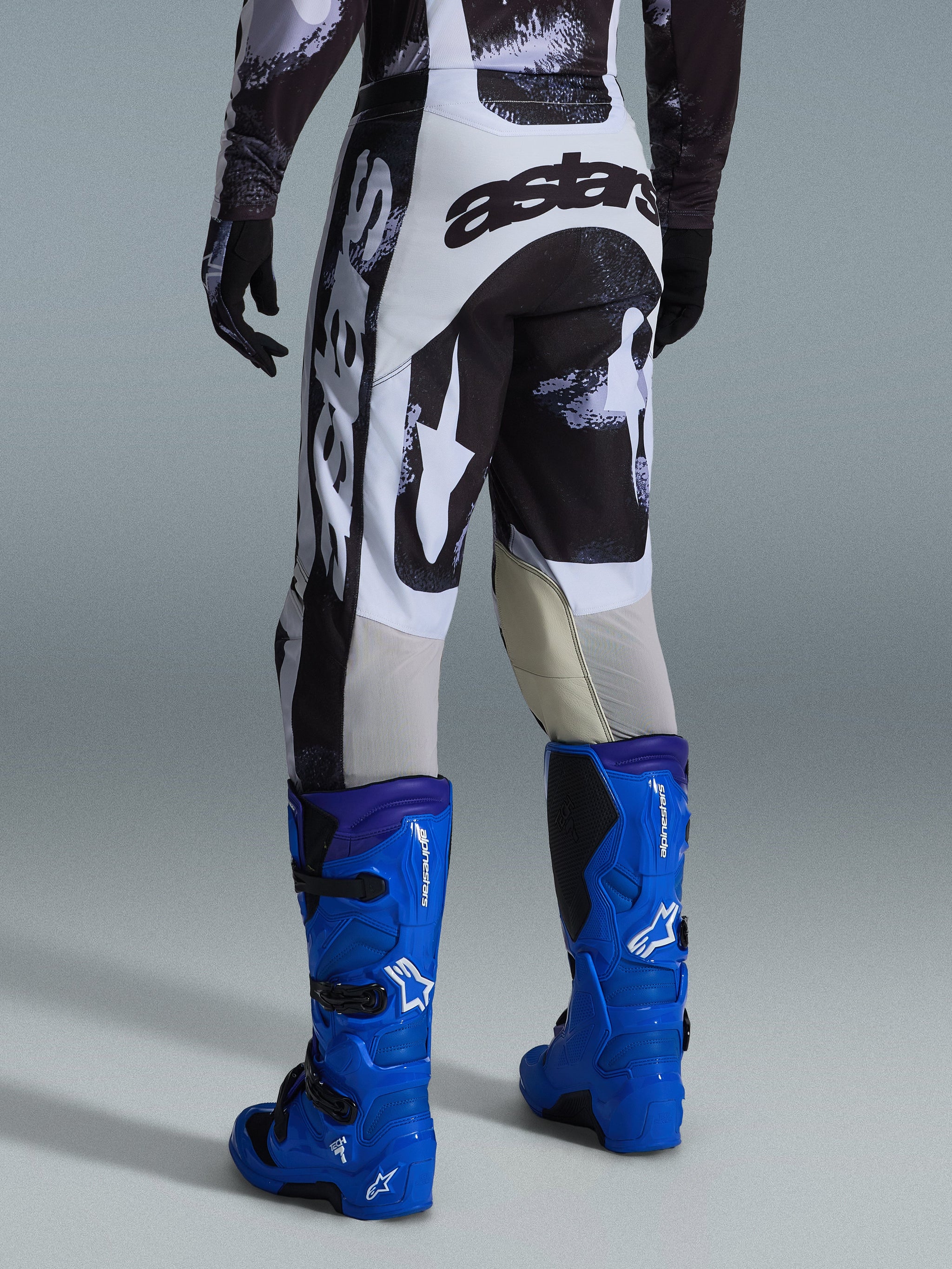 Alpinestars 2026 Racer Lahnd Pants, Motocross Pants, Iron Camo gray and black pattern, back view showing large white and black astars branding, paired with bright blue motocross boots, professional off-road racing gear