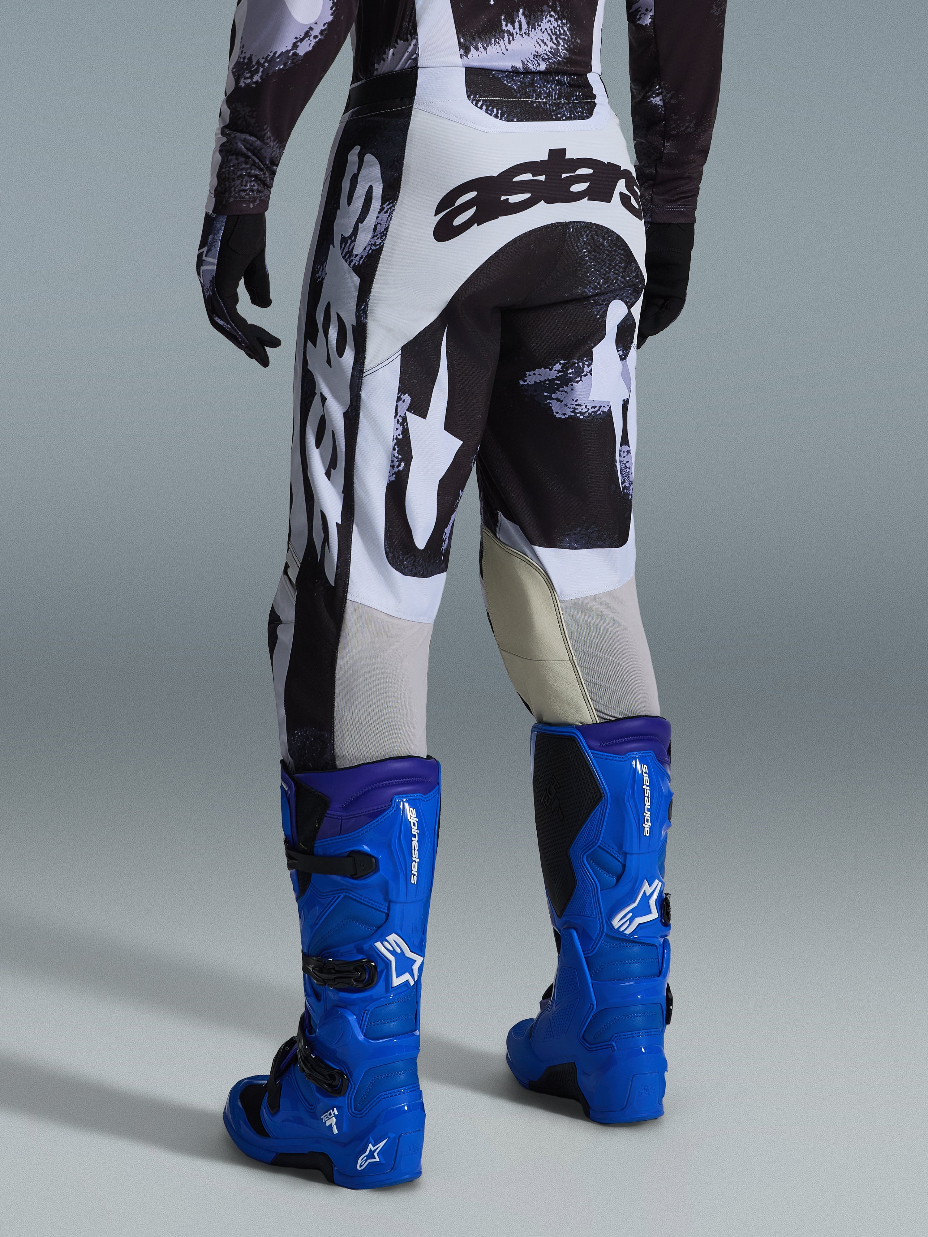 Alpinestars 2026 Racer Lahnd byxor, motocrossbyxor, Iron Camo grått och svart mönster, vy bakifrån som visar stor vit och svart astars-logotyp, kombinerat med klarblå motocross-stövlar, professionell racingutrustning för terrängkörning