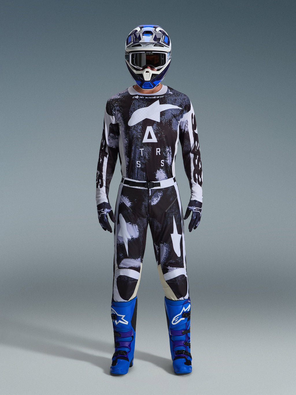 Motocrossförare iklädd Alpinestars 2026 Racer Lahnd-byxor i Iron Camo, grått och svart kamouflagemönster, matchande tröja, blå och vit hjälm med goggles och klarblå stövlar, koordinerat motocross-ställ.