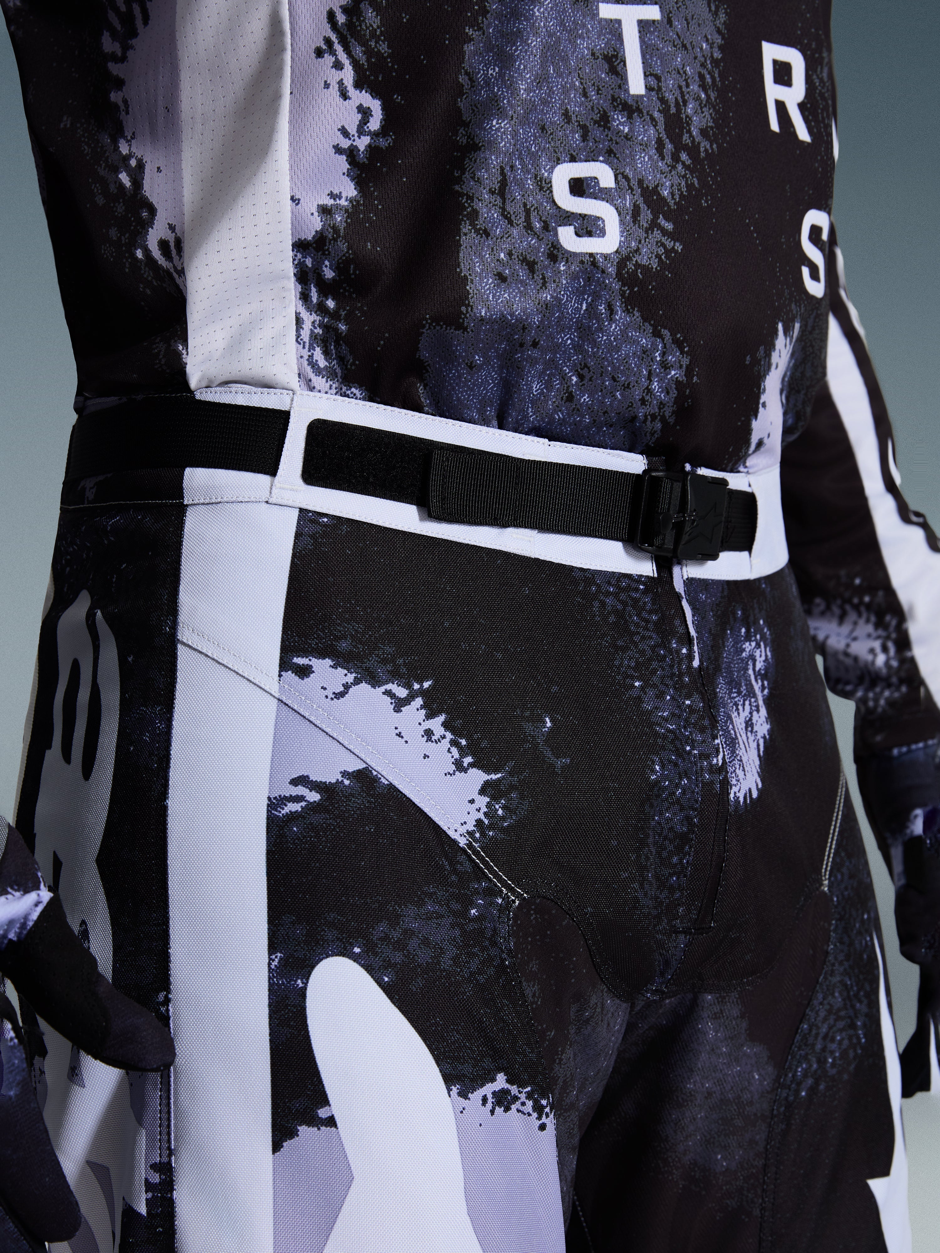 Alpinestars 2026 Racer Lahnd-byxor, motocrossbyxor i Iron Camo, närbild på det justerbara midjebältet och det magnetiska SX2-spännet, med ett grått och svart kamouflagemönster och slitstark konstruktion i 600D-polyväv.