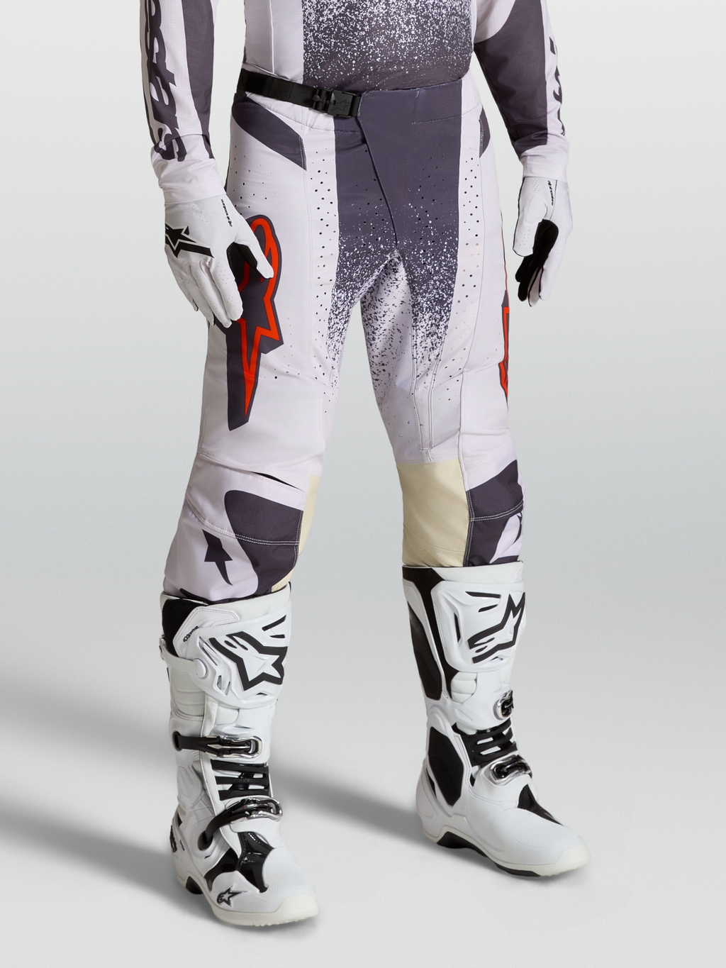 Alpinestars Techstar Swan byxor, motocrossbyxor för herr, ljuslila och mörkgrå med röda fluo-detaljer, modellbild med matchande handskar och vita stövlar för terrängkörning.