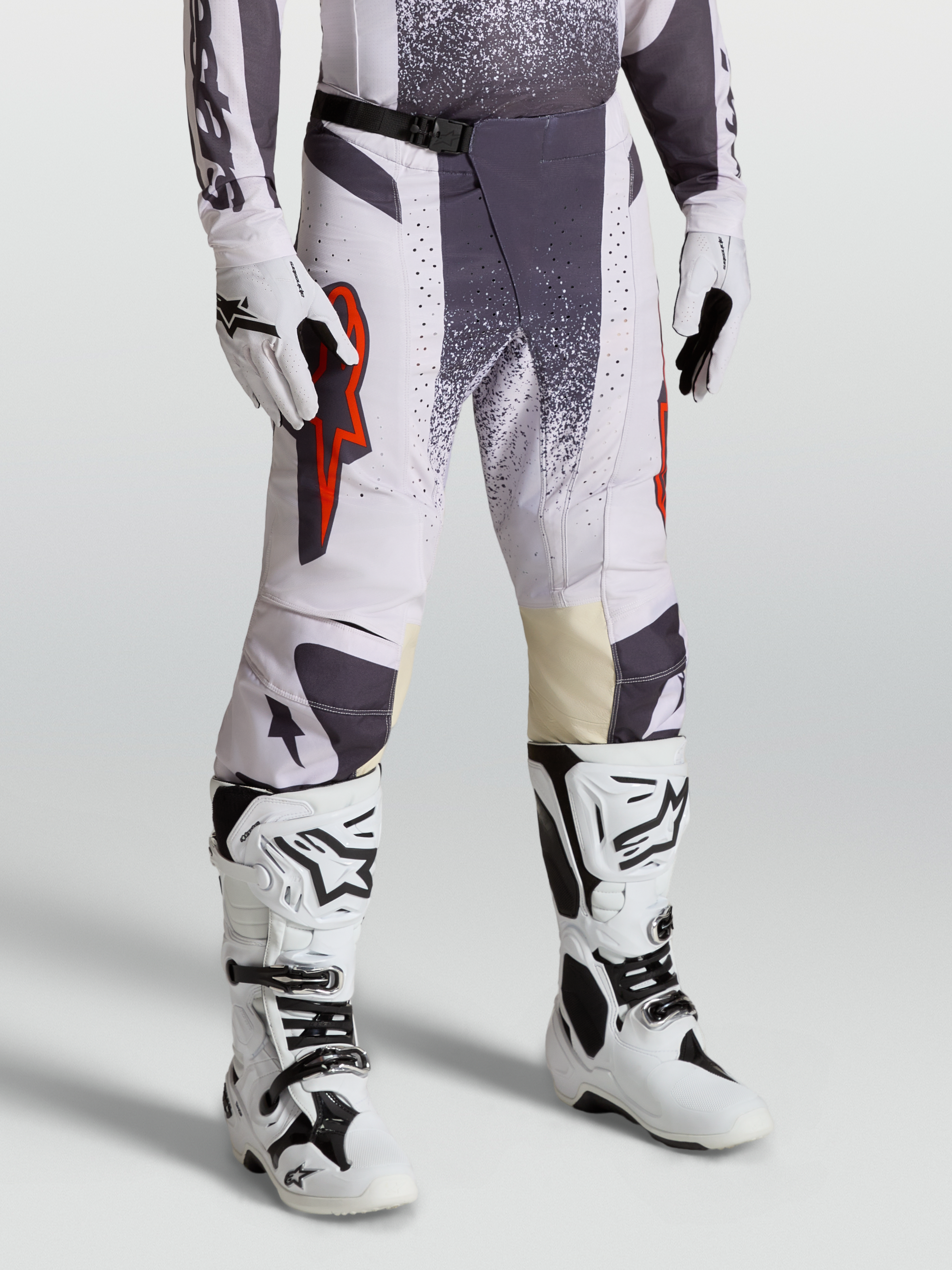 Alpinestars Techstar Swan byxor, motocrossbyxor för herr, ljuslila och mörkgrå med röda fluo-detaljer, modellbild med matchande handskar och vita stövlar för terrängkörning.