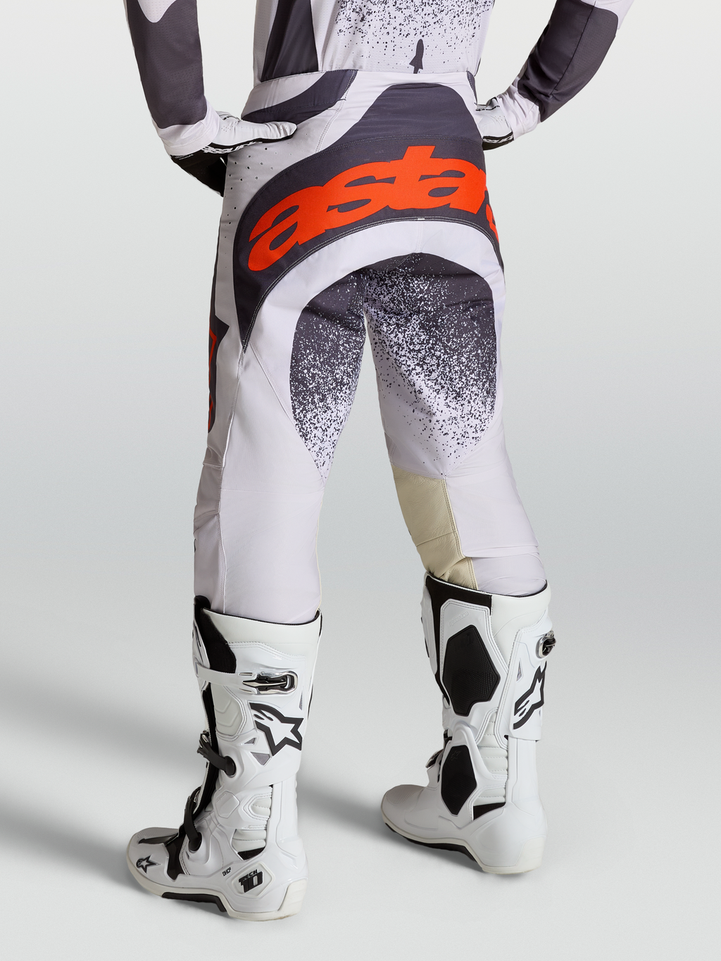 Alpinestars Techstar Swan byxor, motocrossbyxor för herrar, ljuslila och mörkgrå med röd fluo-logotyp, med vita Tech 10 stövlar.