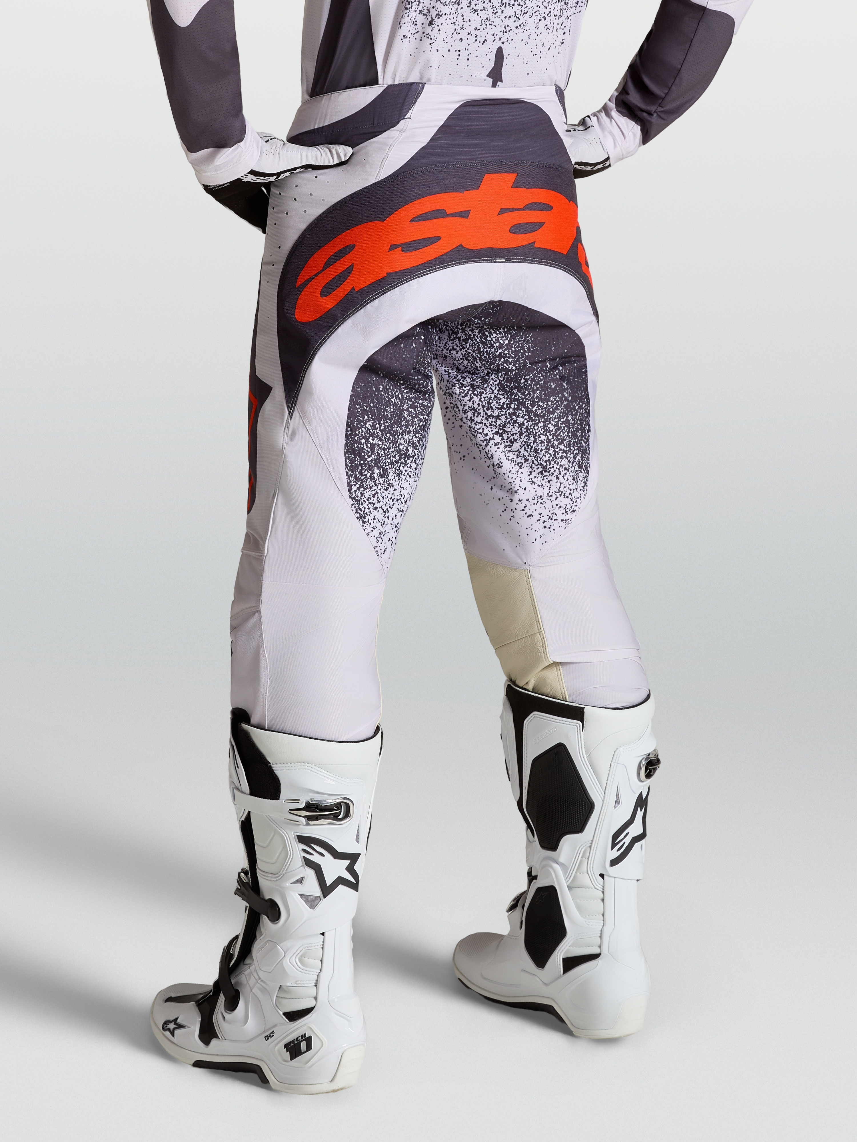 Alpinestars Techstar Swan byxor, motocrossbyxor för herrar, ljuslila och mörkgrå med röd fluo-logotyp, med vita Tech 10 stövlar.