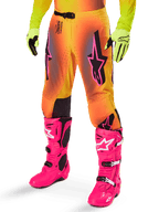 Alpinestars 2025 Supertech Lipan utrustningsset, motocrossbyxor, gul och orange färgövergång med rosa och lila detaljer, framträdande svarta Alpinestars-logotyper på låren, bärs med gula handskar och klarrosa motocross-stövlar.