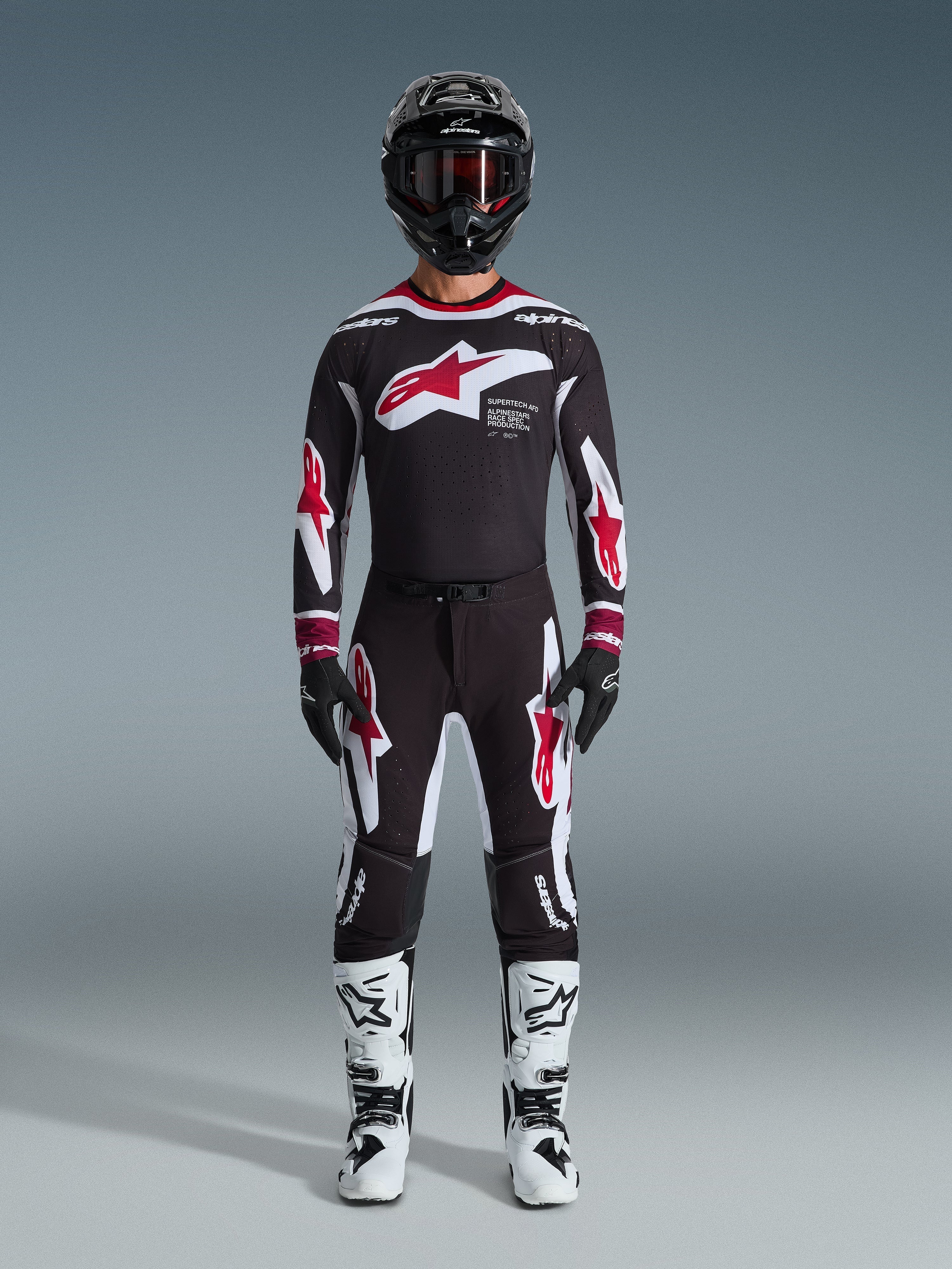 Alpinestars 2026 Supertech AFD Vista byxor, motocrossbyxor, svarta, röda och vita, bärs som ett komplett racingställ med matchande tröja, svart hjälm och vita stövlar, med framträdande röd och vit Astars-logotyp på bröstet och benen, designade för elitprestanda i terräng