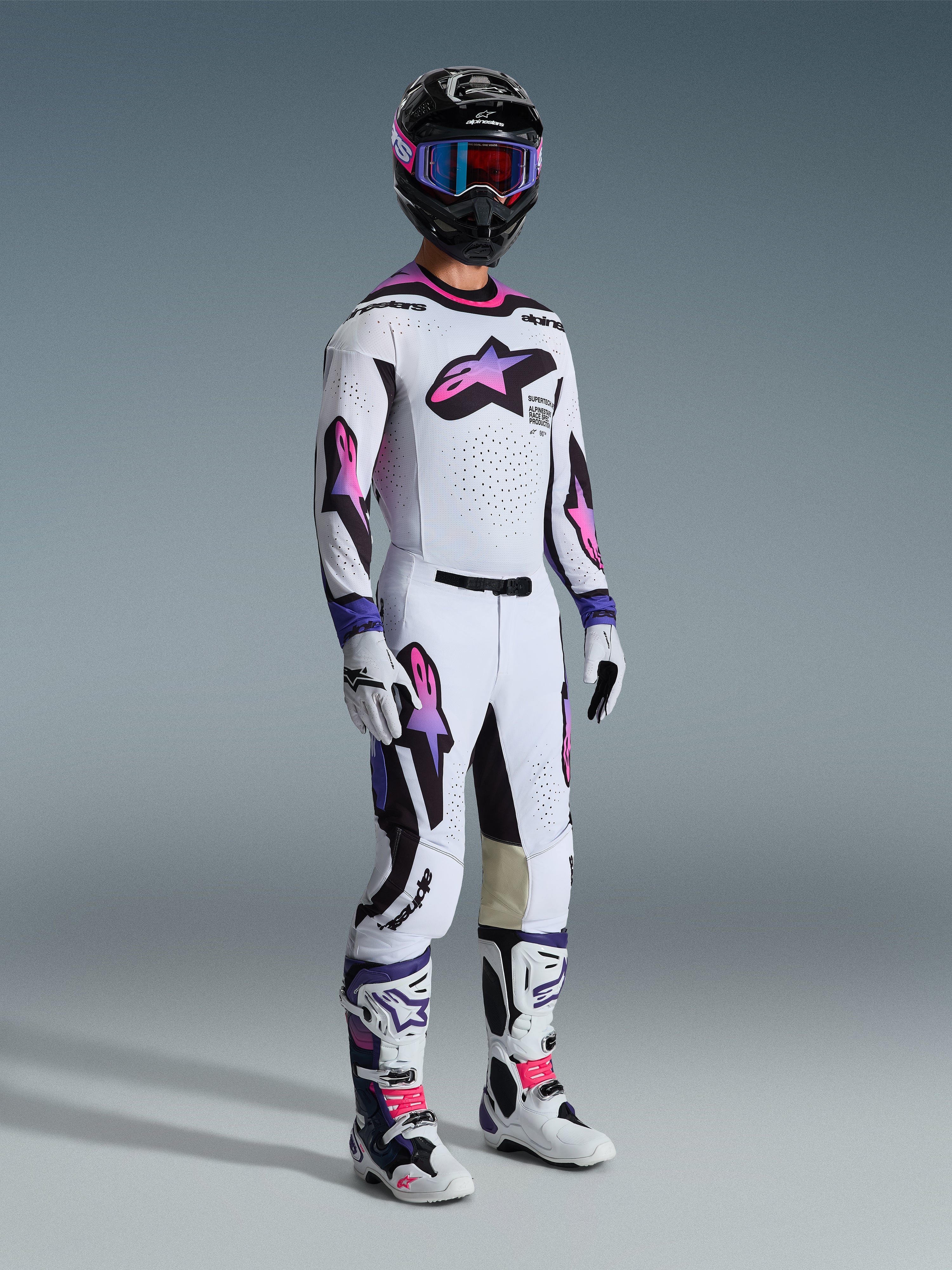 Motocrossförare i komplett racingutrustning, Alpinestars 2026 Supertech AFD Vista Gear Set, vit tröja och byxor med rosa och lila tonade stjärnlogotyper, svarta detaljer, svart hjälm med lila goggles, vita och svarta stövlar med rosa detaljer, koordinerad professionell motocrossoutfit