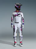 Motocrossförare iklädd Alpinestars 2026 Supertech AFD Vista-utrustningsset, vit tröja och byxor med stjärngrafik i rosa och lila färgövergång, svart hjälm med matchande goggles, vita stövlar med rosa detaljer och vita handskar, koordinerad professionell racingutrustning för terrängkörning