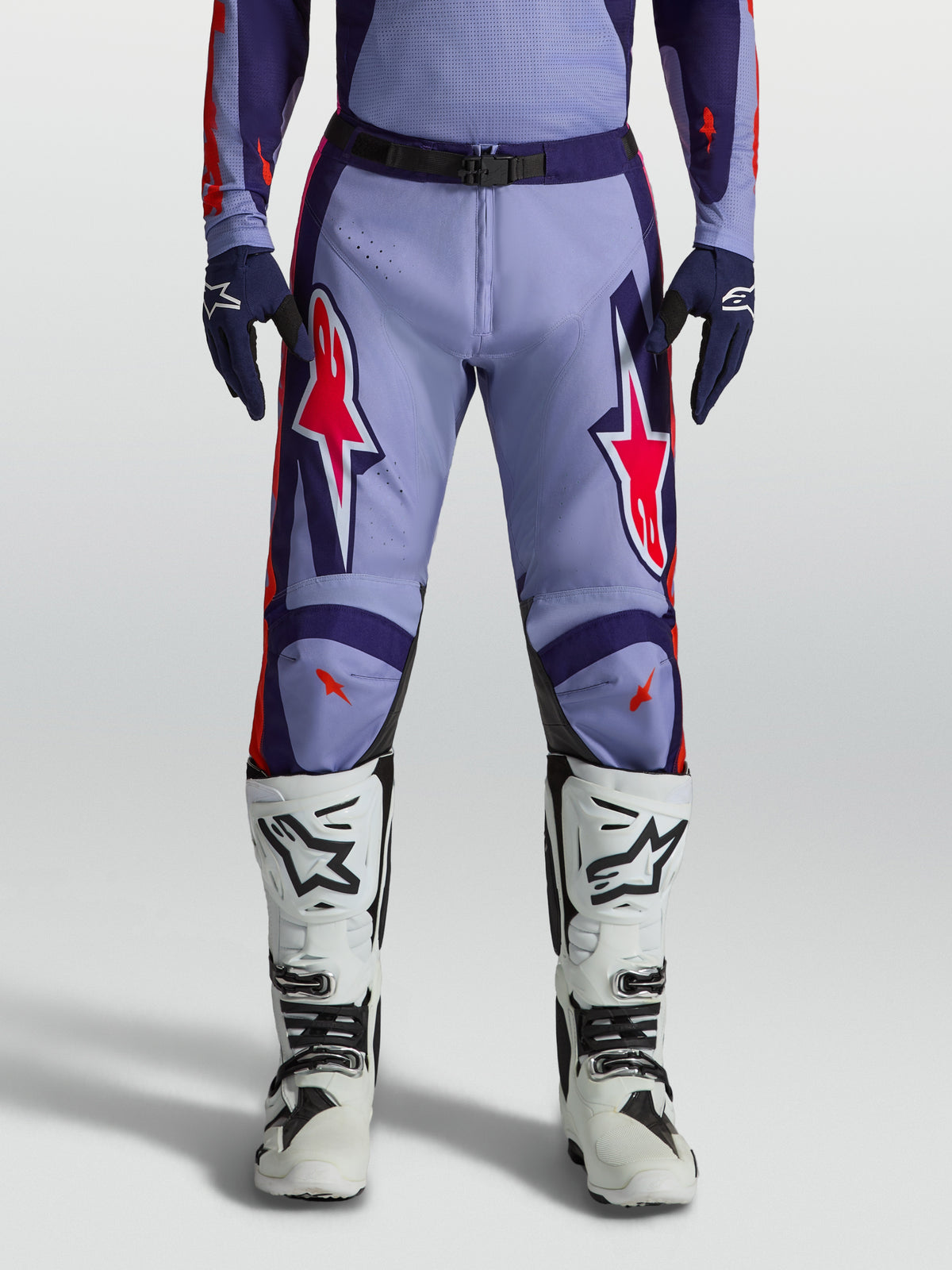Alpinestars Racer Air Hunt motocrossbyxor i lila och violett med neonrosa detaljer, bärs med vita stövlar.