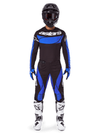 Motocrossförare i Alpinestars 2025 Techstar Dreem utrustningsset, svart tröja med blå bröstpanel och ärmar, matchande svarta och blå byxor, svart hjälm med goggles och vita stövlar, komplett koordinerad motocrossoutfit för terrängkörning.