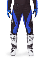 Alpinestars 2025 Techstar Dreem-byxor, motocrossbyxor, svarta och blå, bärs med matchande tröja, handskar och vita stövlar, med blå sidopaneler och atletisk tävlingspassform, hållbart material för terrängkörning