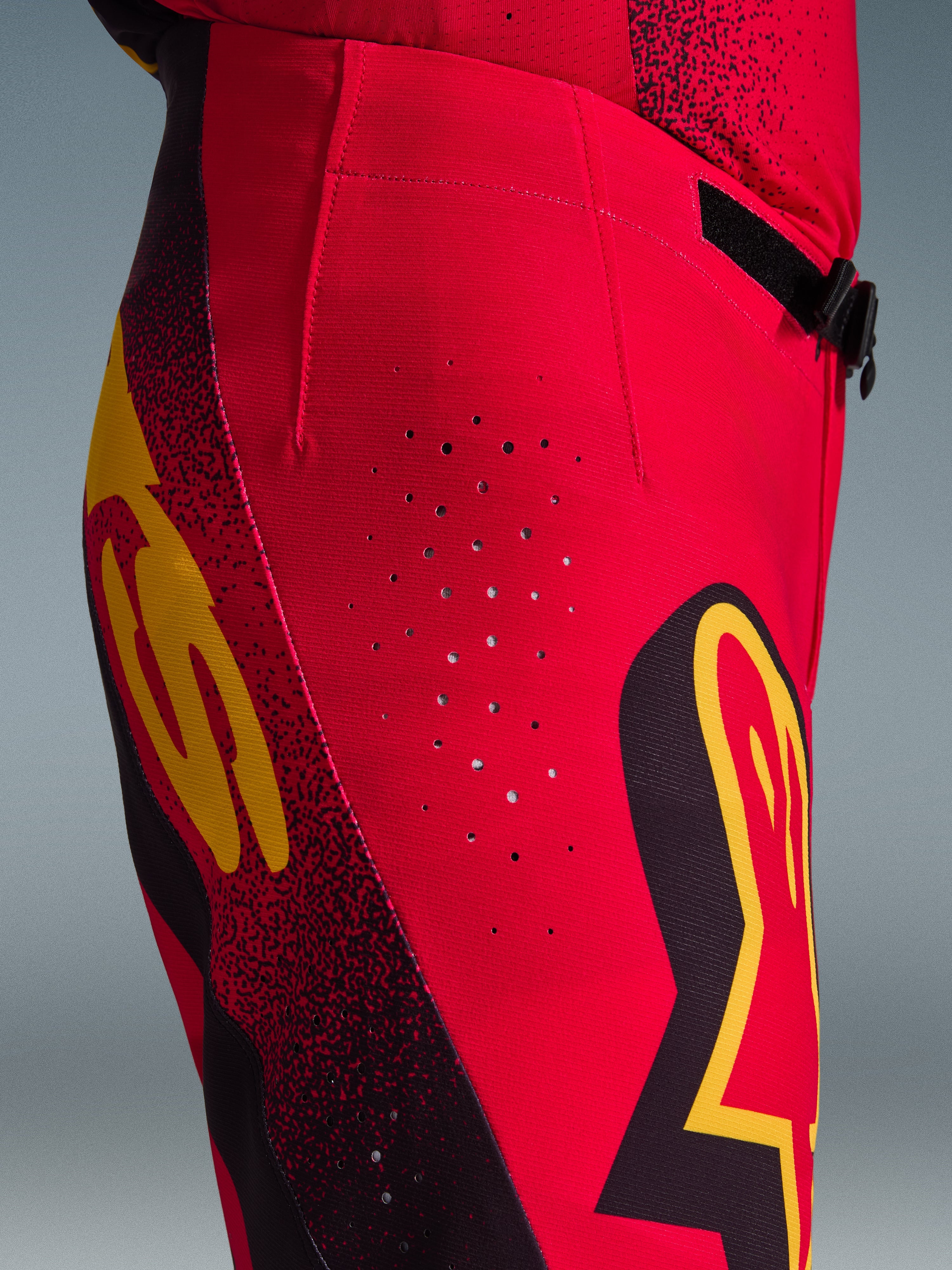 Alpinestars 2026 Supertech Scenz-byxor, motocrossbyxor, röd, svart och gul, närbild från sidan med laserskurna ventilationshål, tydliga grafiska logotyper och högpresterande stretch-ripstop-tyg för motocross.