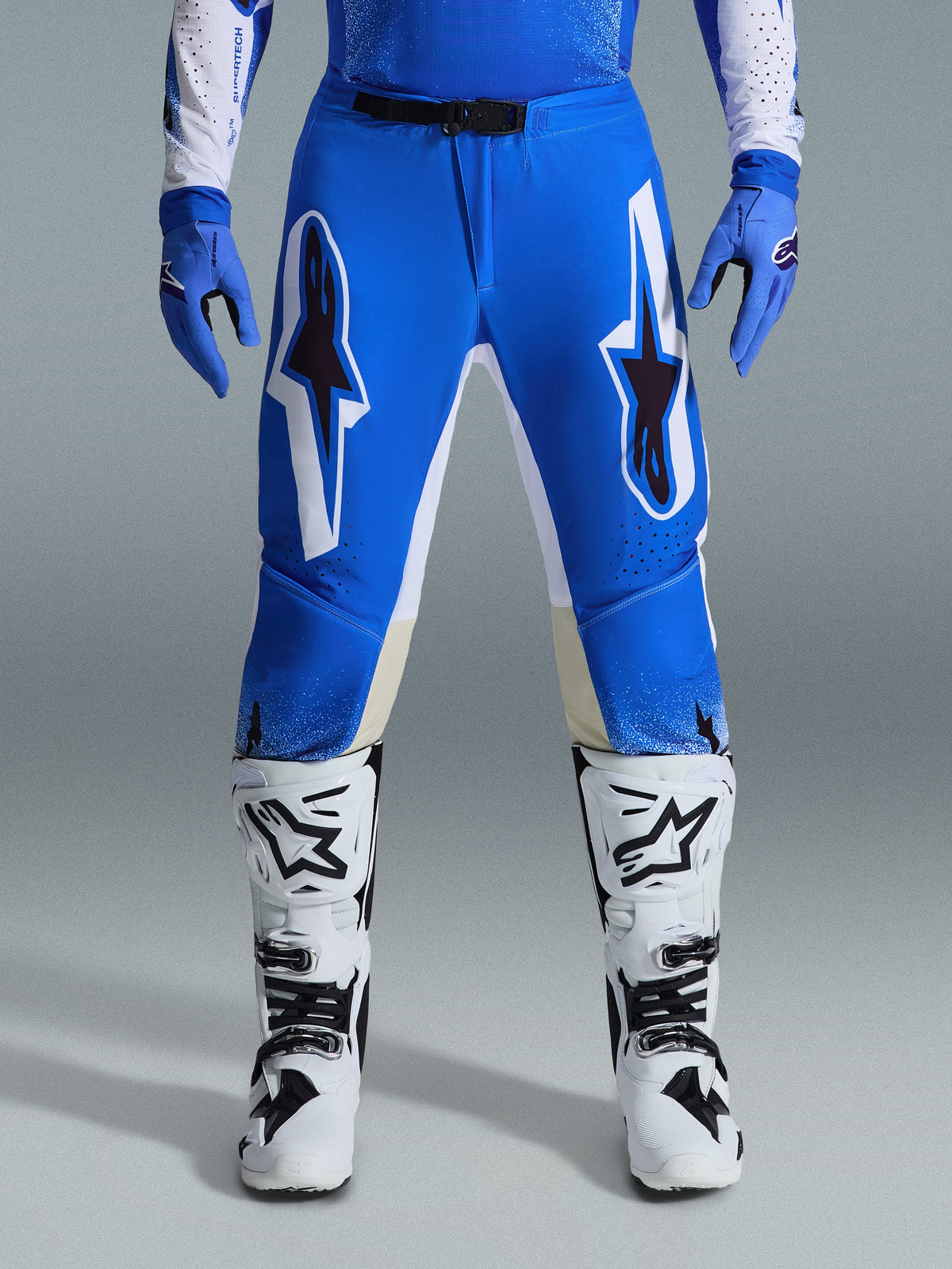 Alpinestars 2026 Supertech Scenz-byxor, motocrossbyxor, Ucla blå och vit, bärs med matchande blå handskar och vita stövlar, med stora vita och svarta grafiska detaljer på låren, atletisk passform för terrängkörning