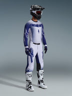 Motocross rider wearing 2026 Supertech Scenz Pants in Light Gray and Dark Blue, matching blue and white jersey with 'astars' branding and spray-paint effect, black helmet with white goggles, white and black motocross boots, coordinated professional off-road racing outfit.