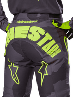 Alpinestars 2025 Racer Hollow byxor, motocrossbyxor, Dark Camo och Yellow Fluo, med en stor gul Alpinestars-logotyp över baksidan, taktiskt kamouflagemönster med klargula accenter och hållbar konstruktion för terrängkörning