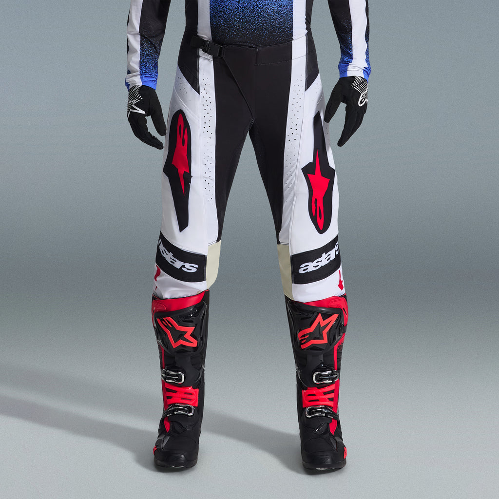 Alpinestars 2026 Techstar Knif-utrustningsset, motocrossutrustning, svarta och vita byxor med stora röda stjärnlogotyper, bärs med svarta och röda racingstövlar och svarta handskar, professionell atletisk passform för offroad-prestanda