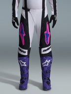 Alpinestars 2026 Techstar Knif Pants, Motocross Racing Pants, Black, White, and Purple with Pink and Blue accents, worn with purple racing boots and black gloves, featuring ergonomic racing cut and bold logo graphics for off-road performance