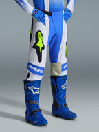 Alpinestars 2026 Techstar Knif-byxor, motocrossbyxor, UCLA-blå, vit och svart med gul fluo, bärs med matchande blå stövlar och handskar, med framträdande Alpinestars-branding och Astar-logotyper, högpresterande utrustning för terrängkörning
