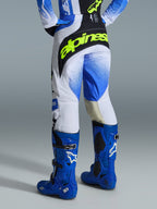 Alpinestars 2026 Techstar Knif byxor, motocrossbyxor, Ucla-blå, svart och neongul, baksida som visar en framträdande neongul Alpinestars-logotyp, vit bas med blå gradientgrafik, bärs med högpresterande klarblå motocross-stövlar.