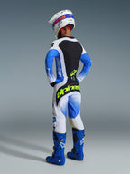 Motocrossförare sedd bakifrån i 2026 Techstar Knif-byxor i färgerna Ucla Blue, svart och neongult, med neongul logotyp på sätet, matchande tröja med blå ärmar, vit hjälm och blå offroad-stövlar.