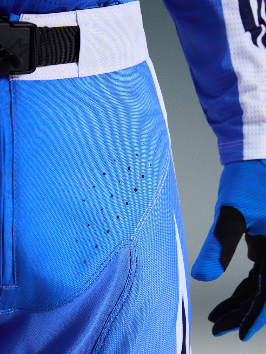 Alpinestars 2026 Techstar Knif-byxor, motocrossbyxor, Ucla-blå och svarta, närbild av lår med laserskurna perforeringar och SX2 magnetiskt midjespänne, teknisk konstruktion för terrängkörning