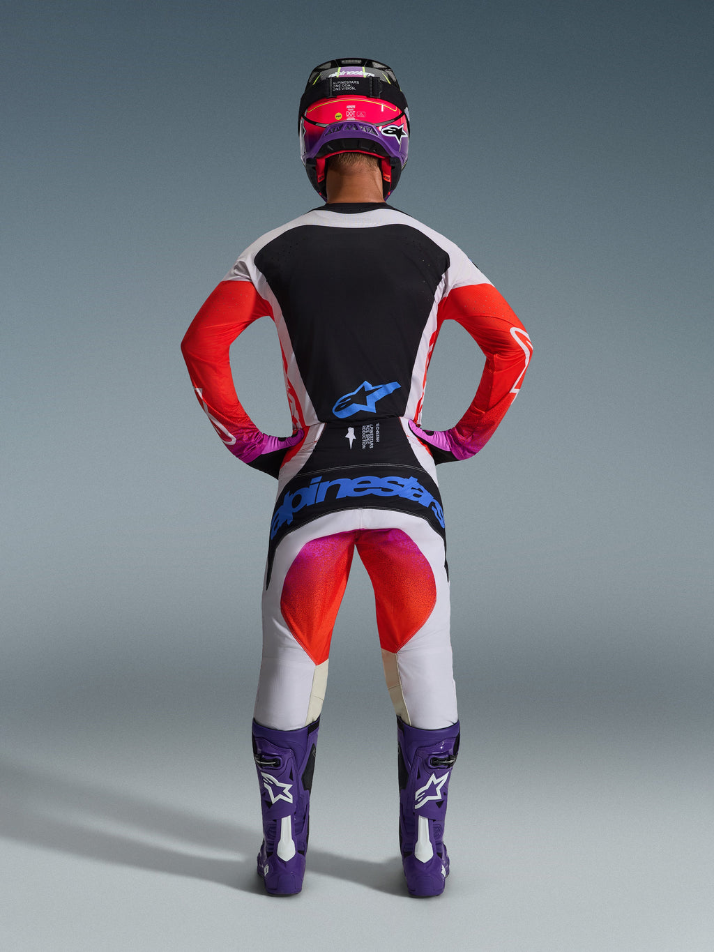 Alpinestars 2026 Techstar Knif Gear Set, complete motocross gear seen from behind, White and Black jersey with red gradient sleeves, White pants with red and pink accents, coordinated with purple boots and pink helmet, bold blue branding, professional off-road racing kit