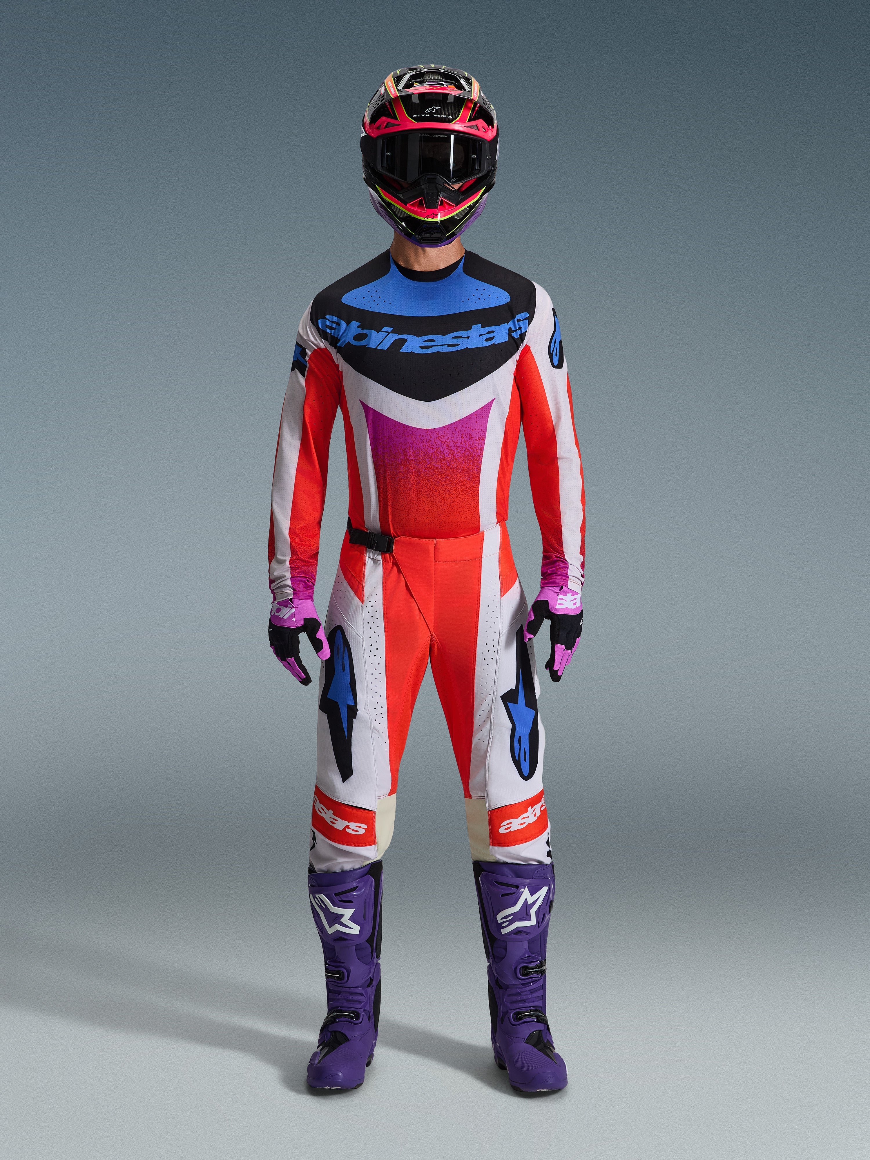 Motocrossförare klädd i 2026 Techstar Knif Gear Set, komplett racingutrustning i rött, vitt och svart med blå logotyper och rosa accenter, lila stövlar med vita logotyper, rosa och svarta handskar samt en svart och rosa hjälm, professionell racingutrustning för terrängkörning