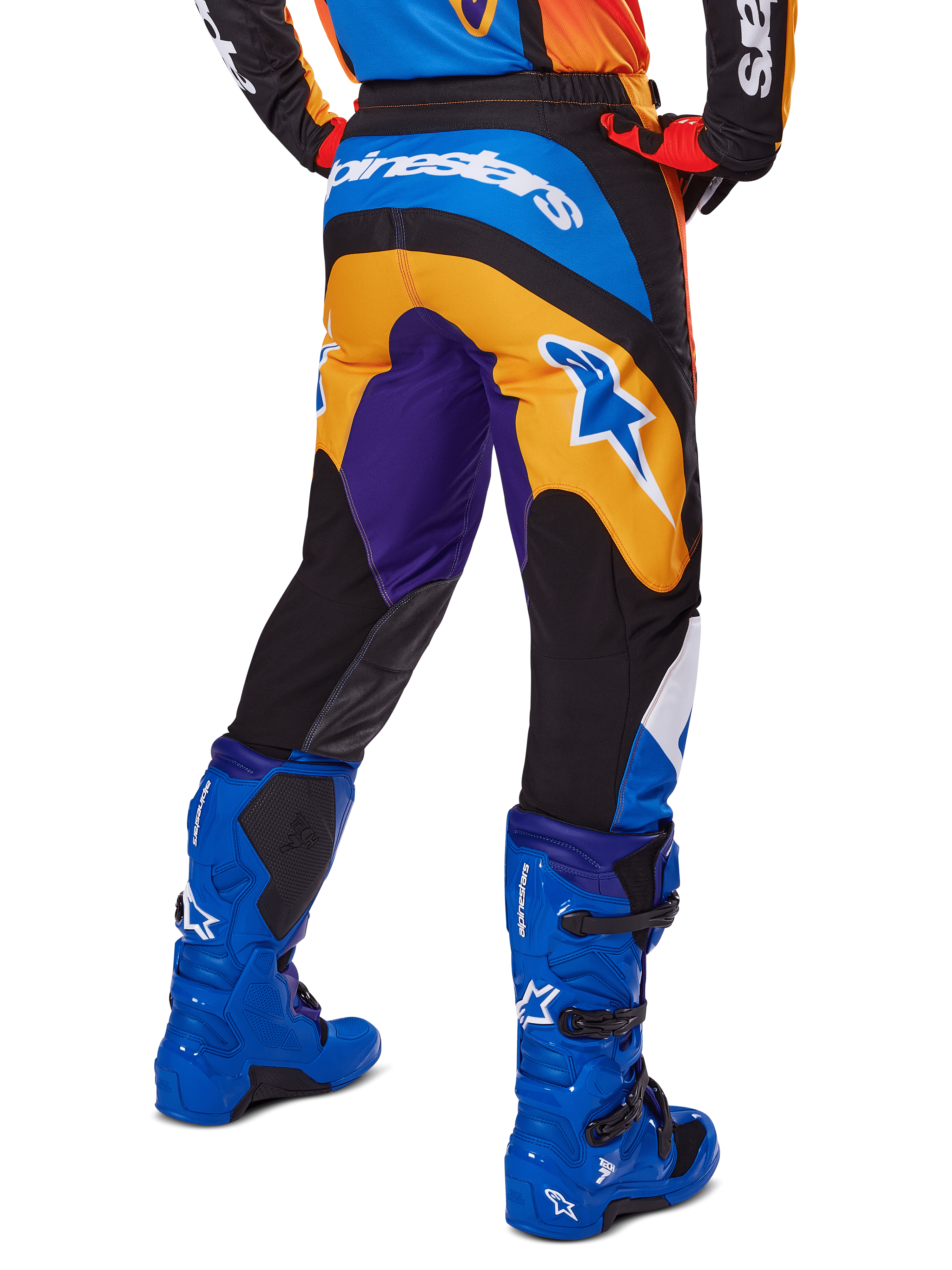 Alpinestars 2025 Fluid Wurx byxor, motocrossbyxor, flerfärgade med orange, lila och blå detaljer, vy bakifrån som visar vit Alpinestars-logotyp på baksidan, matchade med blå motocross-stövlar, atletisk passform för terrängkörning