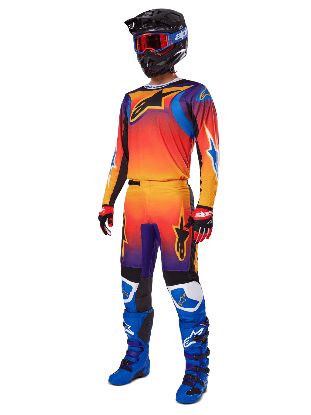 Motocrossförare i komplett racingutrustning, Alpinestars 2025 Fluid Wurx-byxor och matchande tröja med en flerfärgad toning i orange, rött och lila, svart hjälm med röda goggles, blå och svarta stövlar, röda och svarta handskar, koordinerad outfit för terrängkörning
