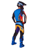 Motocrossförare sedd bakifrån i Alpinestars 2025 Fluid Wurx-byxor, flerfärgad design med blå, orange, gula och lila detaljer, matchande tröja, klart blå stövlar och svart hjälm, komplett utrustning för terrängkörning
