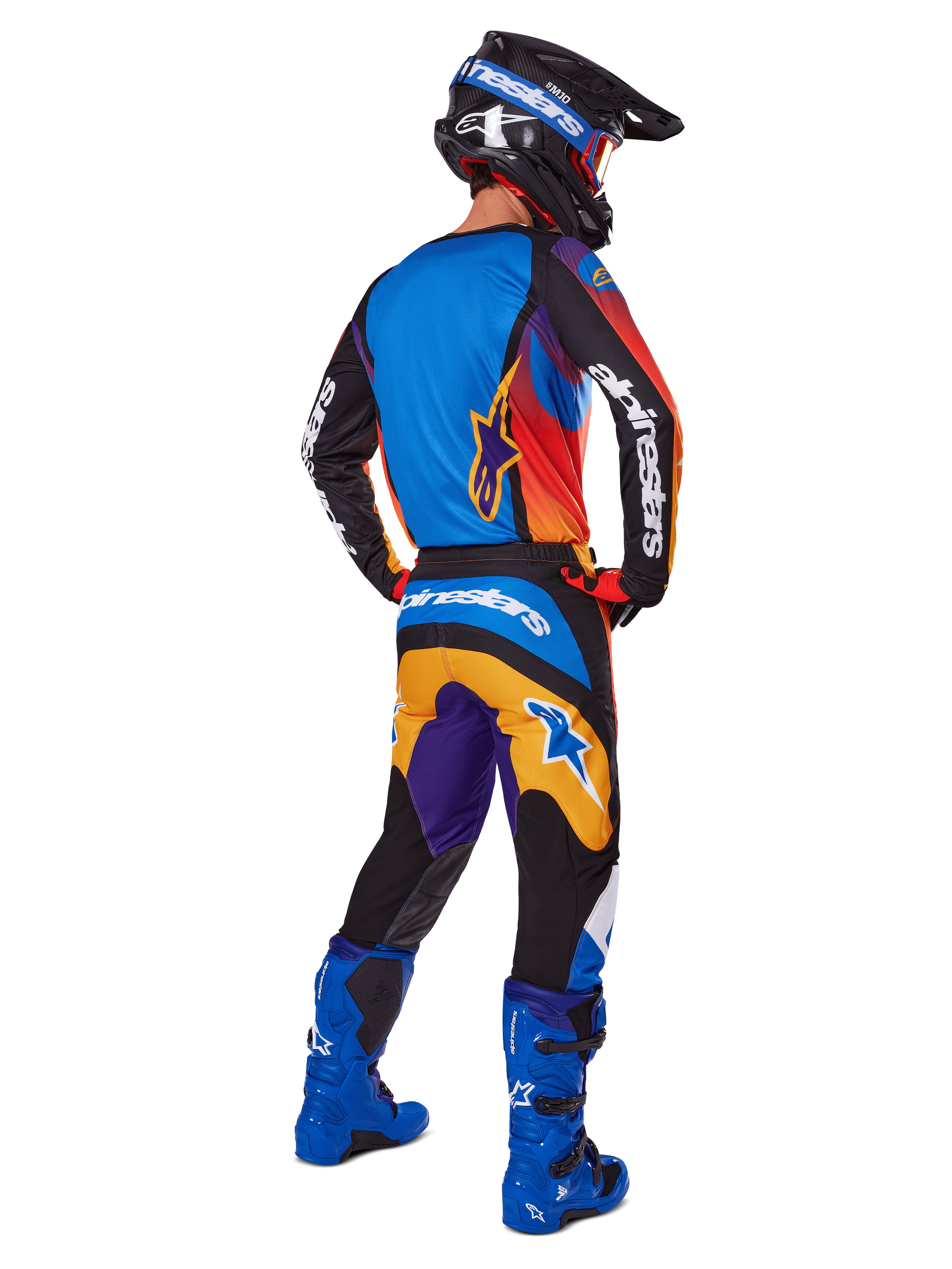 Motocrossförare sedd bakifrån i Alpinestars 2025 Fluid Wurx-byxor, flerfärgad design med blå, orange, gula och lila detaljer, matchande tröja, klart blå stövlar och svart hjälm, komplett utrustning för terrängkörning