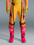Alpinestars 2026 Techstar Nomur-byxor, motocrossbyxor, orange, gula och rosa, bärs med matchande gula handskar och starkt rosa racingstövlar, med svarta paneler och framträdande rosa Alpinestars-logotyp, teknisk racingutrustning för terrängkörning