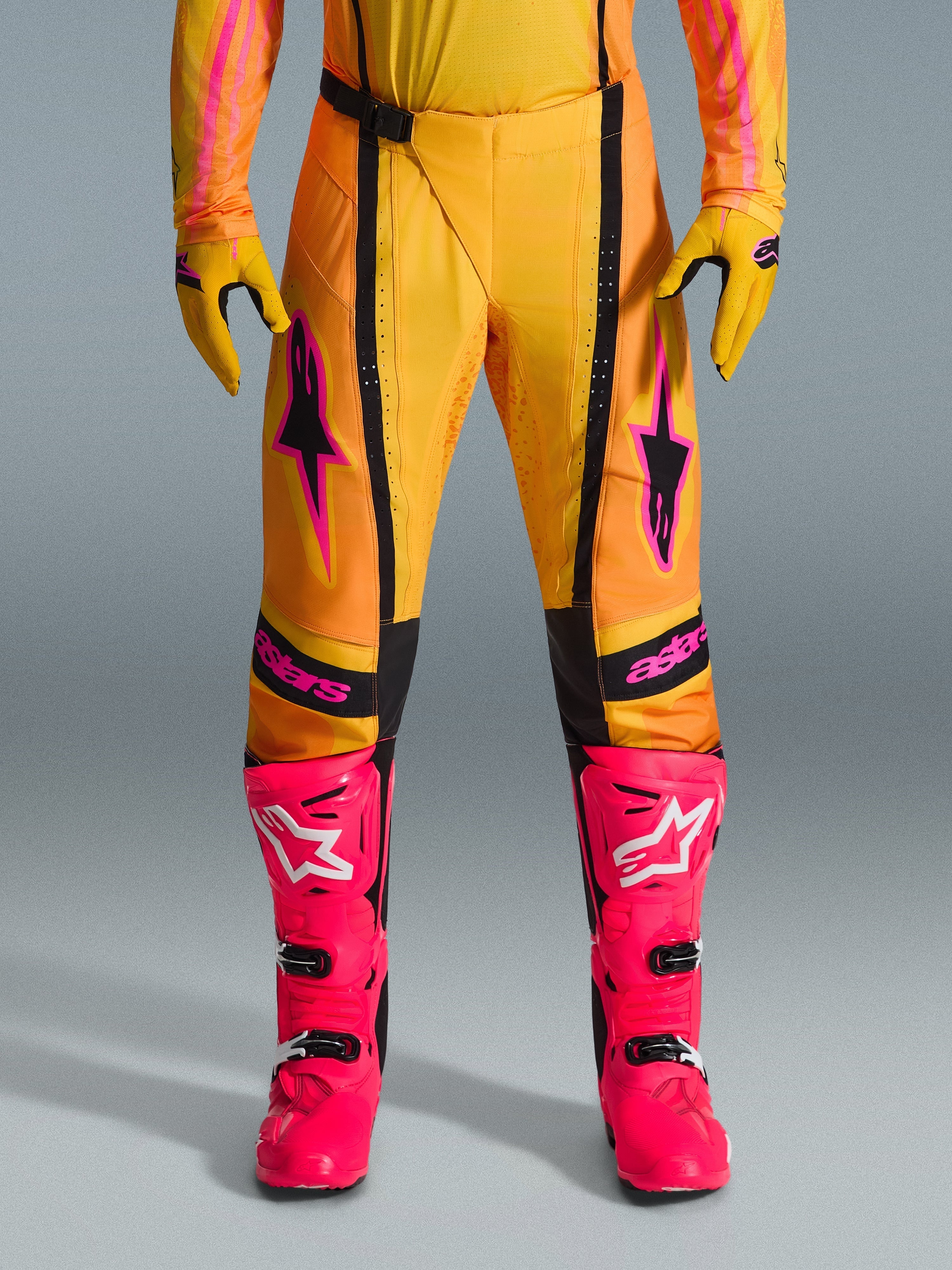 Alpinestars 2026 Techstar Nomur-byxor, motocrossbyxor, orange, gula och rosa, bärs med matchande gula handskar och starkt rosa racingstövlar, med svarta paneler och framträdande rosa Alpinestars-logotyp, teknisk racingutrustning för terrängkörning