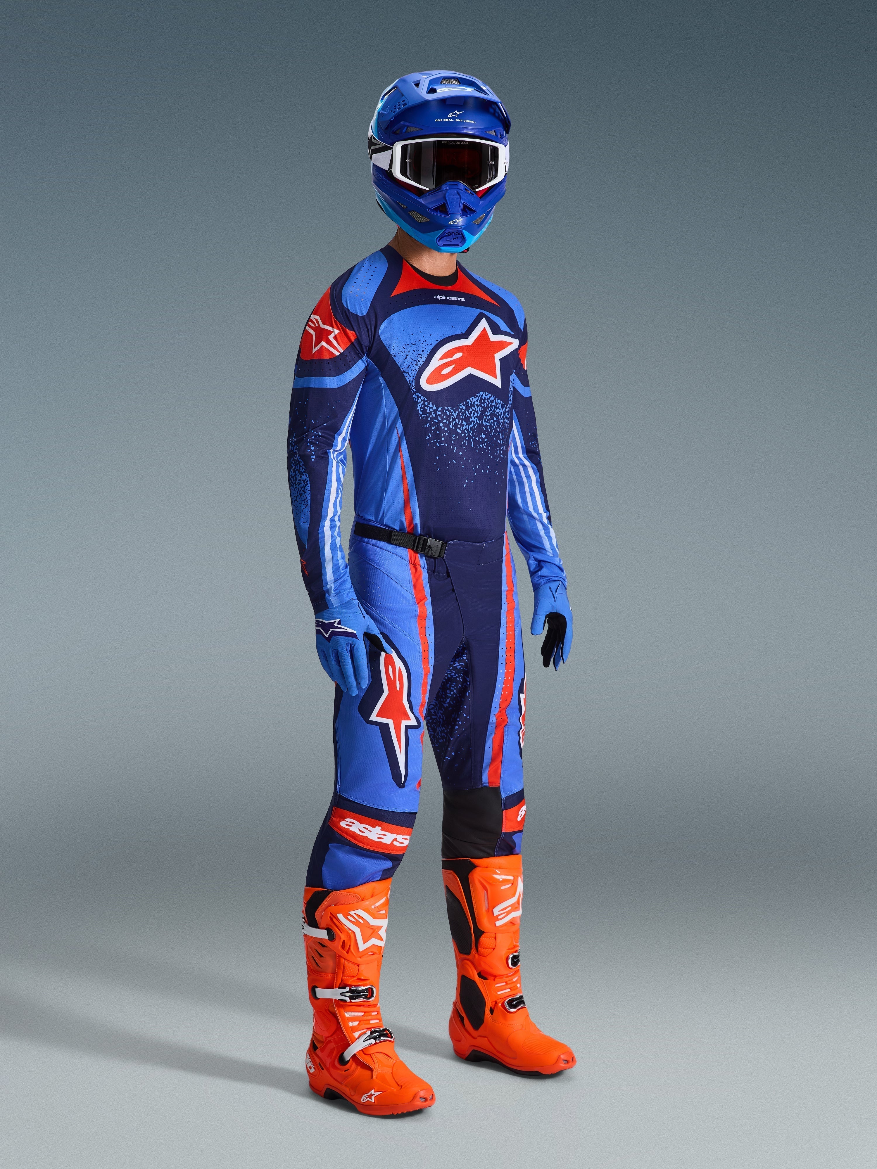 Alpinestars 2026 Techstar Nomur-byxor, motocrossbyxor, mörkblå, orange och UCLA-blå, bärs av en förare i komplett racingutrustning inklusive matchande tröja, blå hjälm och klarorangea stövlar, prestandakonstruerade för terrängkörning