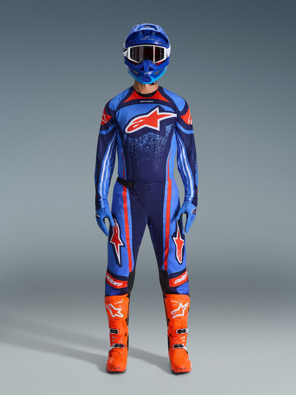 Alpinestars 2026 Techstar Nomur utrustningsset, motocrossförare i komplett racingutrustning, mörk marinblå med orangea och UCLA-blå detaljer, matchande tröja och byxor med stora logotyper, blå hjälm och klarorangea stövlar, koordinerad tävlingsutrustning för terrängkörning