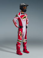 Motocrossförare i komplett racingutrustning, 2026 Techstar Nomur-tröja i rött, vitt och svart, matchande motocrossbyxor med gula detaljer, svart hjälm med goggles, röda stövlar och svarta handskar, koordinerad outfit för terrängkörning