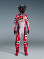 Alpinestars 2026 Techstar Nomur tröja, röd och vit med svarta detaljer och gula logotyper, bärs av en motocrossförare med matchande byxor, röda stövlar och en svart hjälm, professionell terrängkörningsutrustning