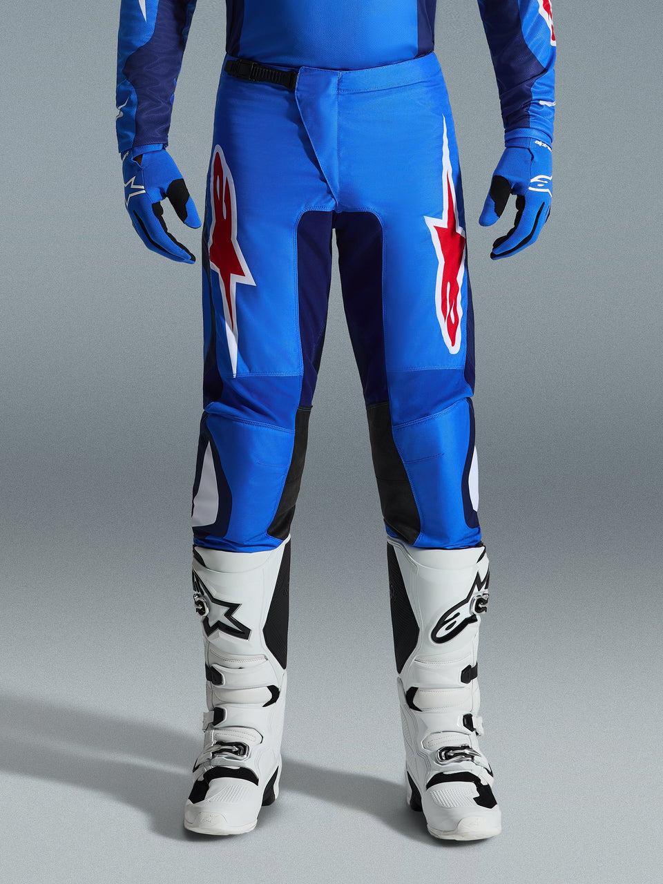 Alpinestars 2026 Fluid Grid byxor, motocrossbyxor, blå och röda, med framträdande röda och vita stjärnlogotyper på låren, bärs med matchande blå handskar och vita offroad-stövlar, atletisk passform med hållbara paneler för racing.