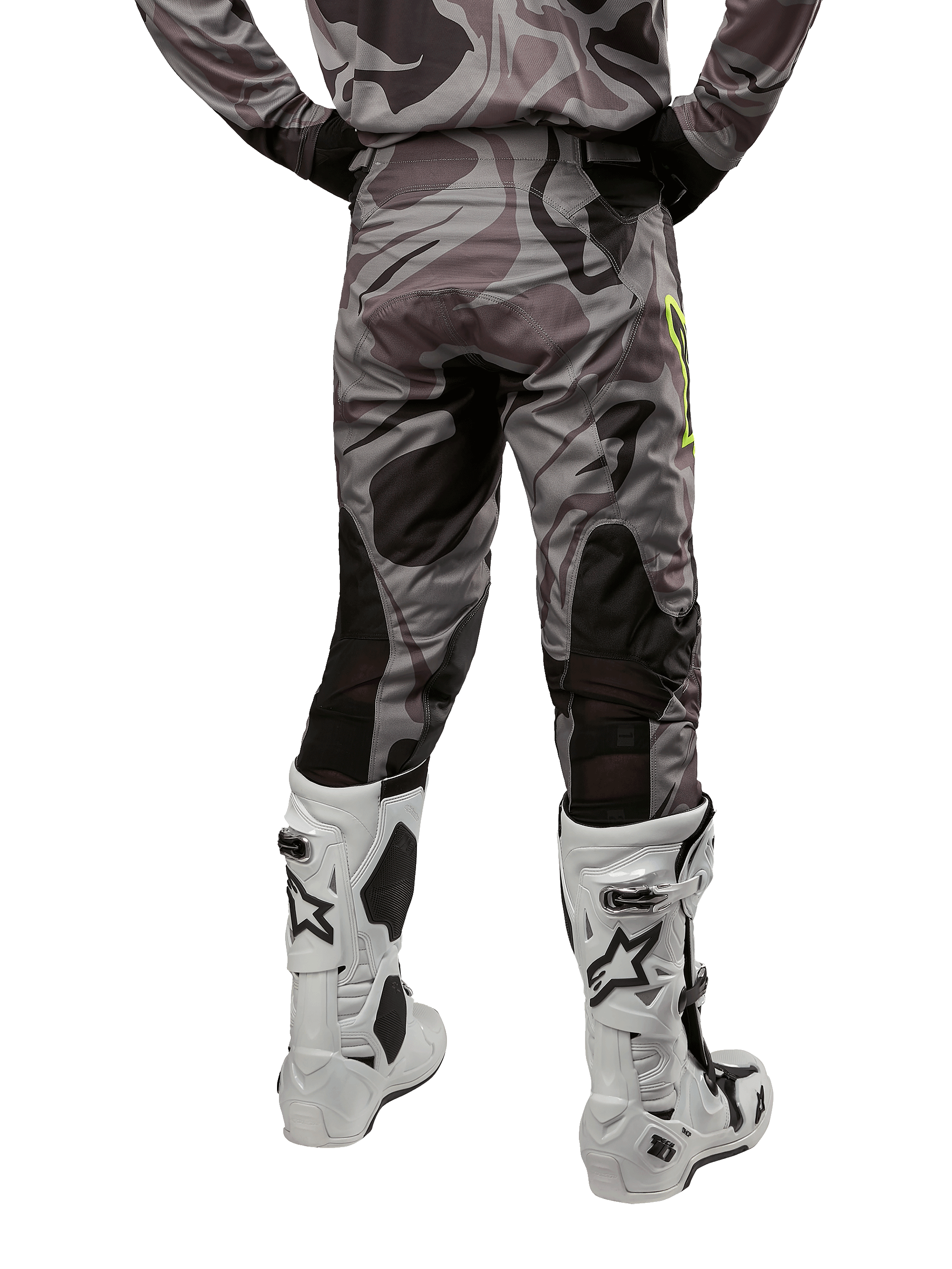 Alpinestars 2024 Racer Tactical byxor, motocrossbyxor, Cast Gray Camo Magnet, baksida som visar kamouflagemönstret och svarta andningsbara stretchzoner, bärs med vita och svarta motocross-stövlar, designade för terrängkörning