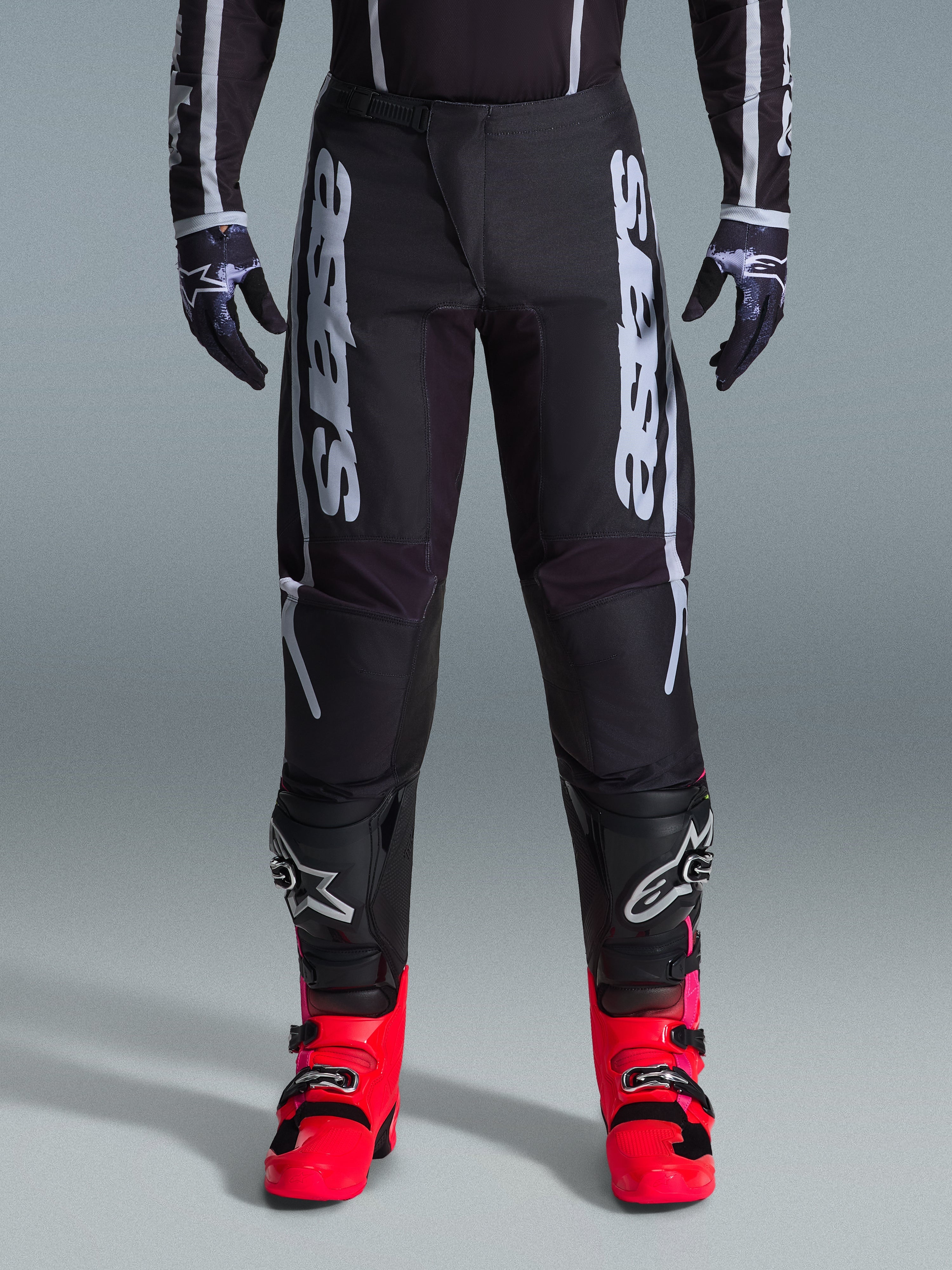 Alpinestars 2026 Fluid Apex Pants, Black Motocross Pants with large White Lettering, worn with black knee protection and vibrant red boots, lightweight 600D polyfabric chassis, sport-fit design for off-road racing