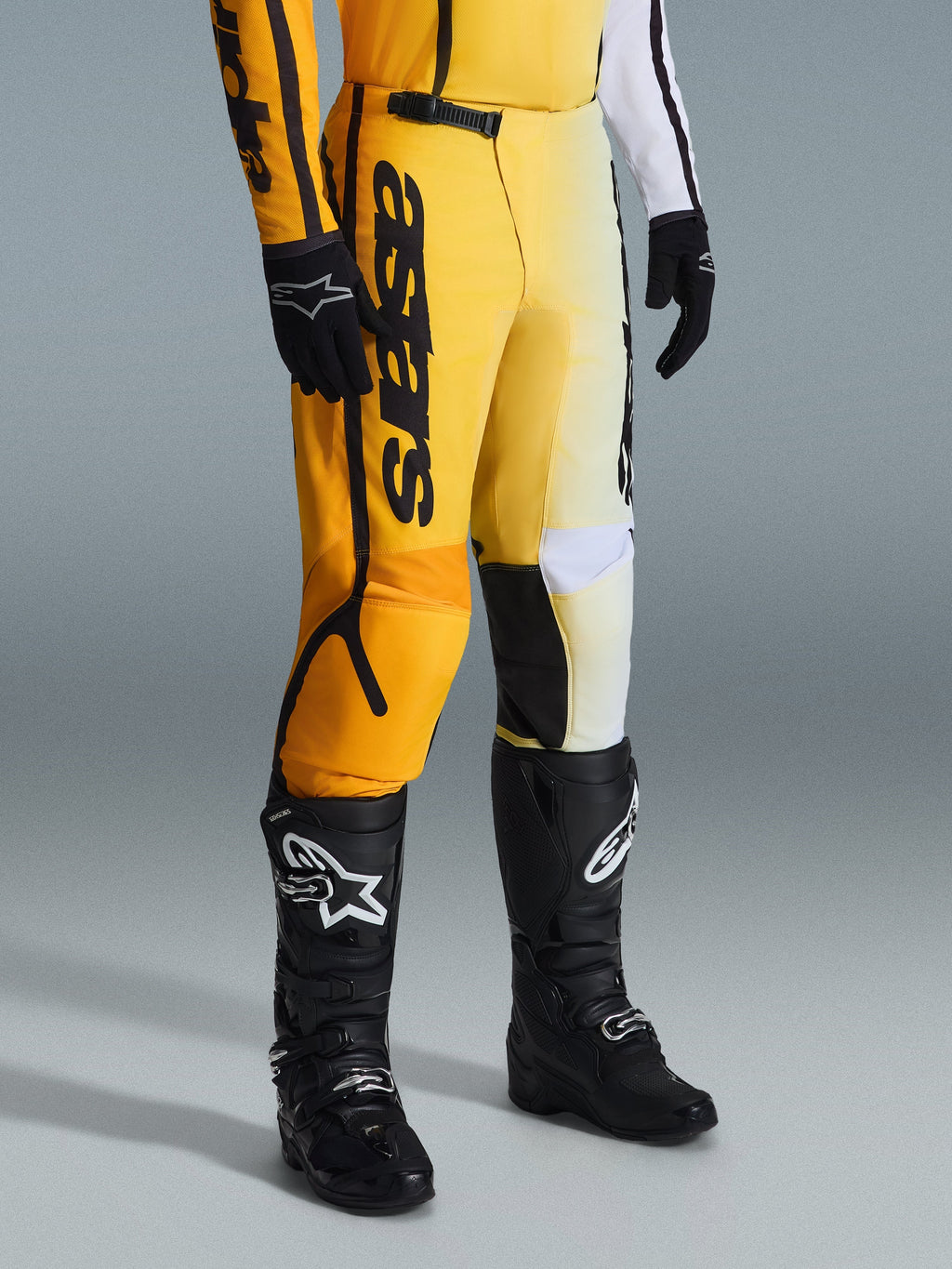 Alpinestars 2026 Fluid Apex byxor, motocrossbyxor, gul och svart, bärs med svarta stövlar och handskar, med tydlig 'astars'-logotyp på låret, ergonomisk design med förstärkta paneler, hållbart material för terrängkörning