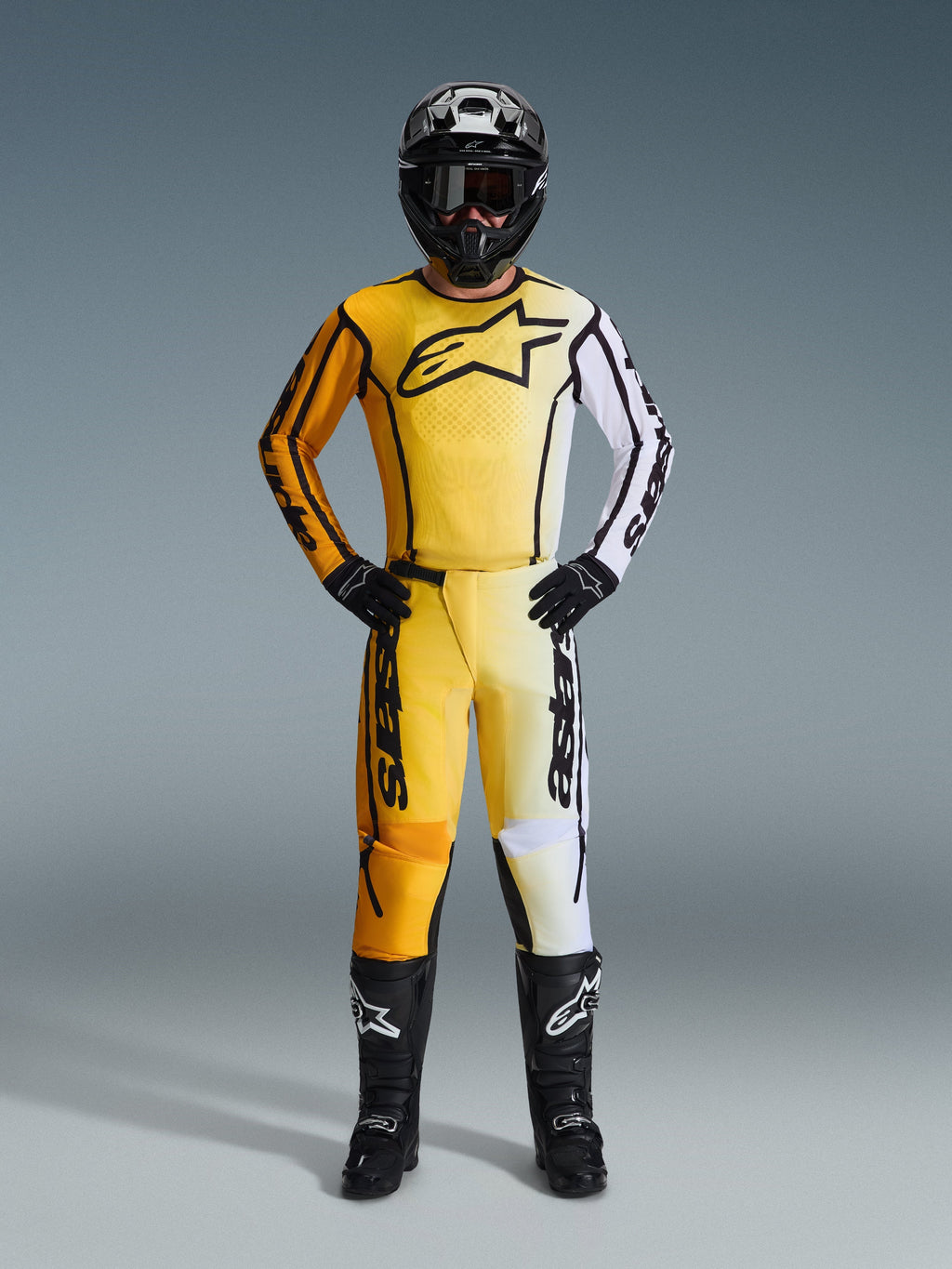 Alpinestars 2026 Fluid Apex byxor, motocrossbyxor i gult, svart och vitt, bärs som ett komplett racingkit med matchande gradienttröja, svart hjälm och stövlar, professionell utrustning för terrängkörning.