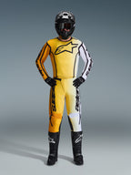 Alpinestars 2026 Fluid Apex byxor, motocrossbyxor i gult, svart och vitt, bärs som ett komplett racingkit med matchande gradienttröja, svart hjälm och stövlar, professionell utrustning för terrängkörning.