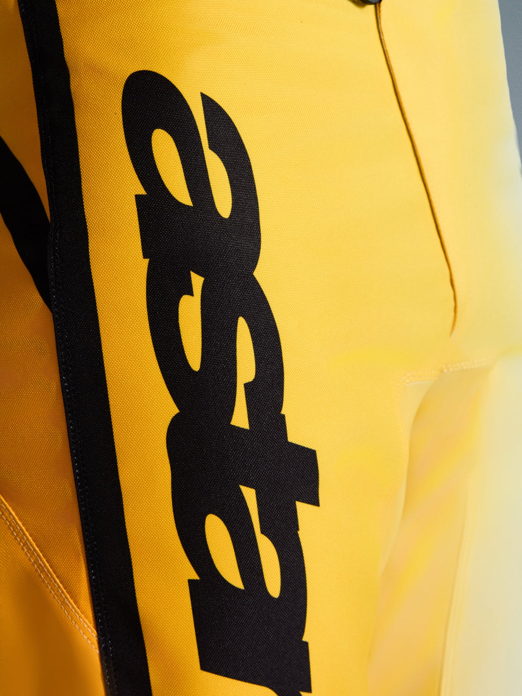 Närbild på Alpinestars 2026 Fluid Apex byxor, motocrossbyxor, gula och svarta, med en stor vertikal svart logotyp, texturerat slitstarkt material och ergonomiska detaljer för terrängprestanda